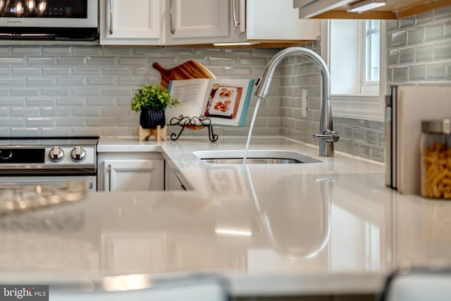 kitchen with light countertops, backsplash, stainless steel range with electric cooktop, white cabinets, and a sink