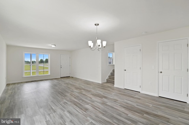 empty room with a chandelier, baseboards, light wood finished floors, and stairs