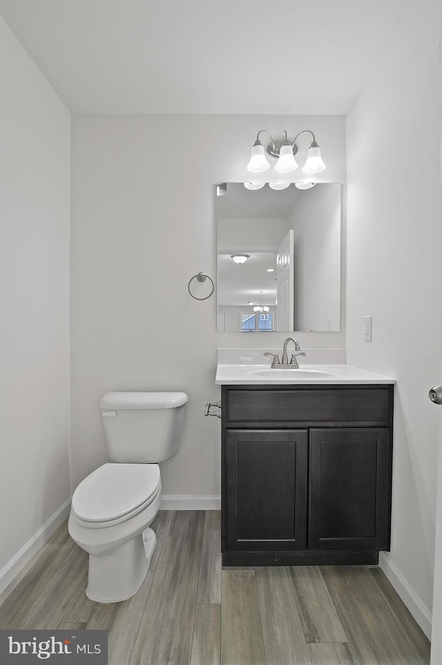 half bath featuring toilet, baseboards, wood finished floors, and vanity