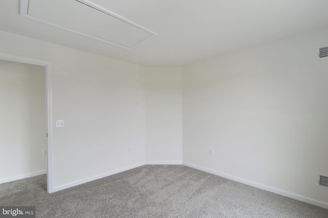 carpeted empty room with attic access, visible vents, and baseboards