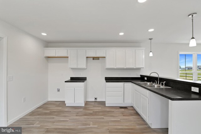 kitchen with light wood-type flooring, white cabinetry, sink, kitchen peninsula, and pendant lighting