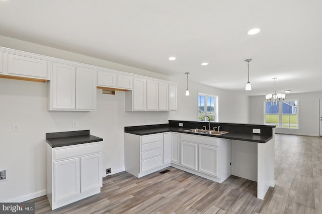 kitchen with white cabinets, light wood-type flooring, a notable chandelier, sink, and pendant lighting