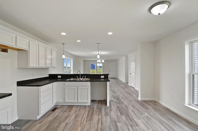 kitchen with decorative light fixtures, kitchen peninsula, sink, light wood-type flooring, and white cabinets