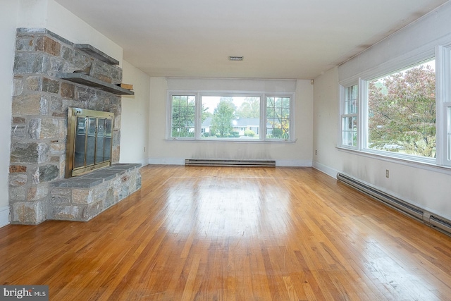 unfurnished living room featuring light wood-type flooring, a stone fireplace, and a baseboard heating unit