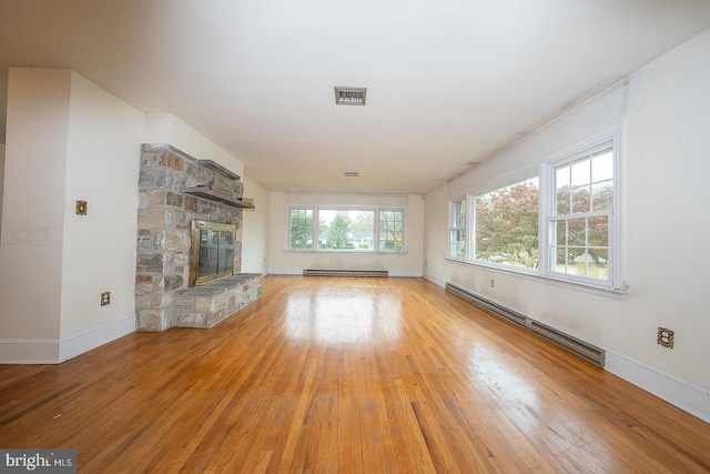 unfurnished living room with a stone fireplace, a baseboard radiator, and light hardwood / wood-style flooring