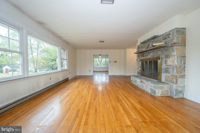 unfurnished living room featuring a stone fireplace, baseboard heating, and light hardwood / wood-style floors