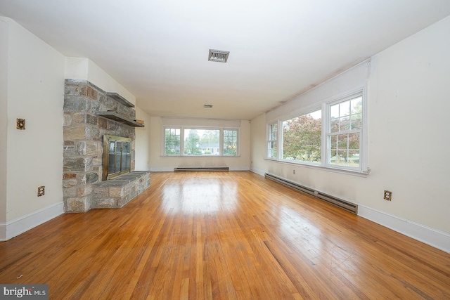 unfurnished living room featuring light hardwood / wood-style flooring, a baseboard heating unit, a healthy amount of sunlight, and a stone fireplace