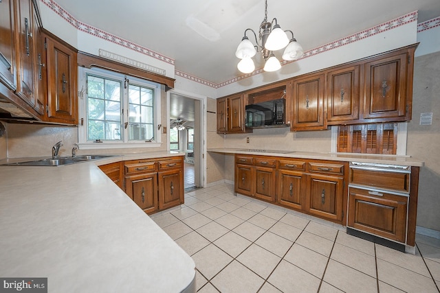 kitchen featuring ceiling fan with notable chandelier, light tile patterned floors, pendant lighting, cooktop, and sink