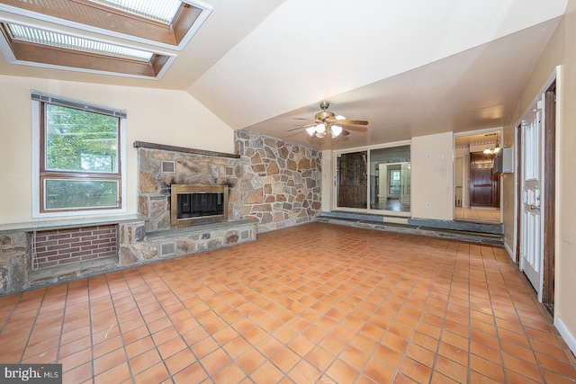 unfurnished living room with vaulted ceiling with skylight, tile patterned flooring, ceiling fan, and a fireplace