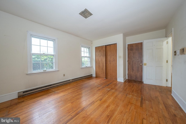 unfurnished bedroom featuring a baseboard heating unit, light hardwood / wood-style floors, and multiple windows