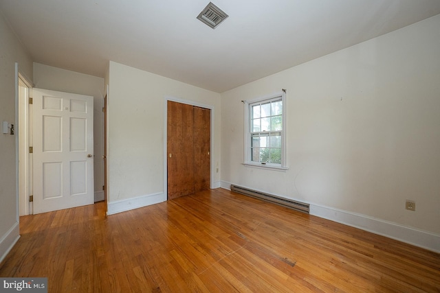 unfurnished bedroom with light hardwood / wood-style flooring, a closet, and baseboard heating