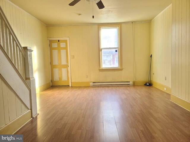 unfurnished room with light hardwood / wood-style flooring, baseboard heating, wooden walls, and ceiling fan