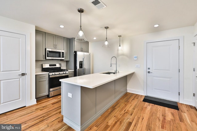 kitchen featuring pendant lighting, light hardwood / wood-style flooring, kitchen peninsula, sink, and appliances with stainless steel finishes