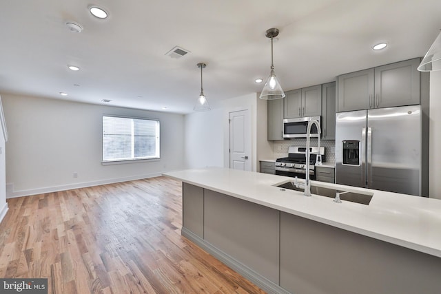 kitchen with gray cabinetry, backsplash, decorative light fixtures, stainless steel appliances, and light hardwood / wood-style floors