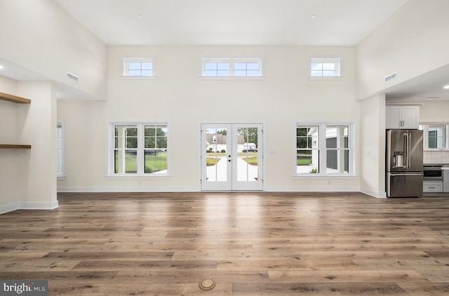 unfurnished living room with hardwood / wood-style floors, a high ceiling, plenty of natural light, and french doors