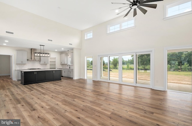 unfurnished living room with recessed lighting, visible vents, a high ceiling, light wood-type flooring, and baseboards