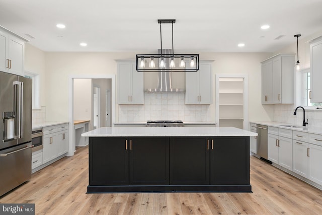 kitchen featuring wall chimney exhaust hood, a kitchen island, stainless steel appliances, light wood-type flooring, and a sink