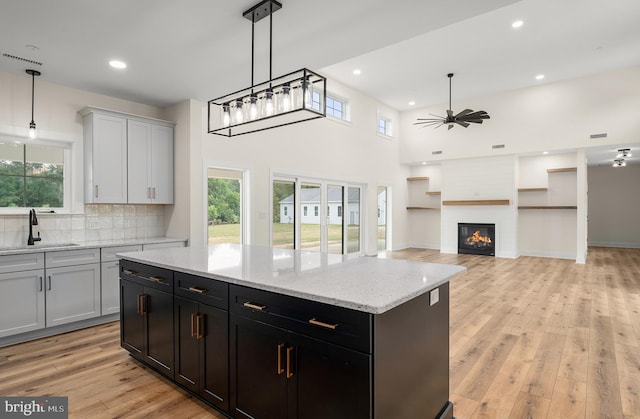 kitchen featuring a fireplace, light wood finished floors, backsplash, a sink, and ceiling fan