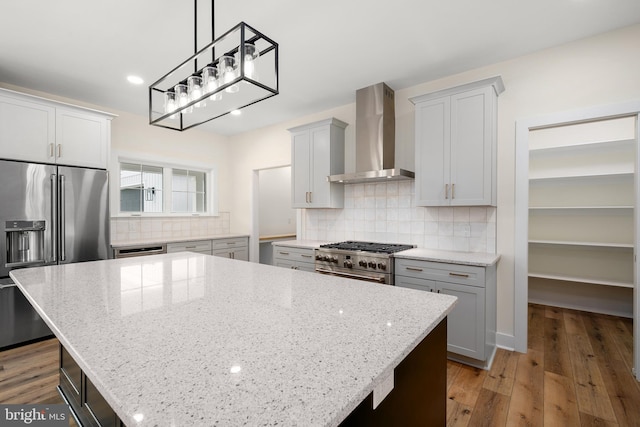 kitchen featuring dark wood-type flooring, wall chimney exhaust hood, high quality appliances, and a center island