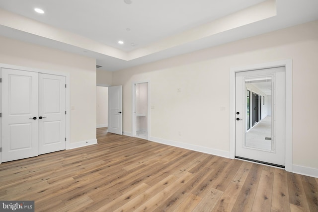 empty room featuring light wood-style floors, baseboards, a raised ceiling, and recessed lighting