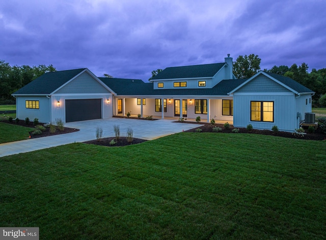 view of front of property with an attached garage, cooling unit, driveway, a front lawn, and a chimney