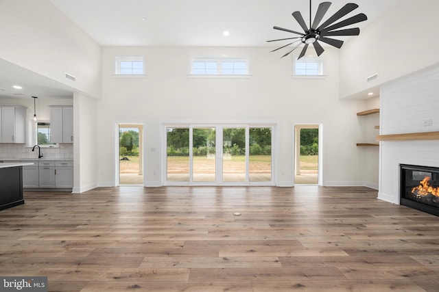 unfurnished living room with light wood-type flooring, a healthy amount of sunlight, a glass covered fireplace, and baseboards