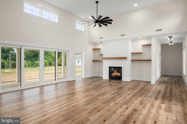 unfurnished living room with ceiling fan, a fireplace, visible vents, light wood-style floors, and a wealth of natural light