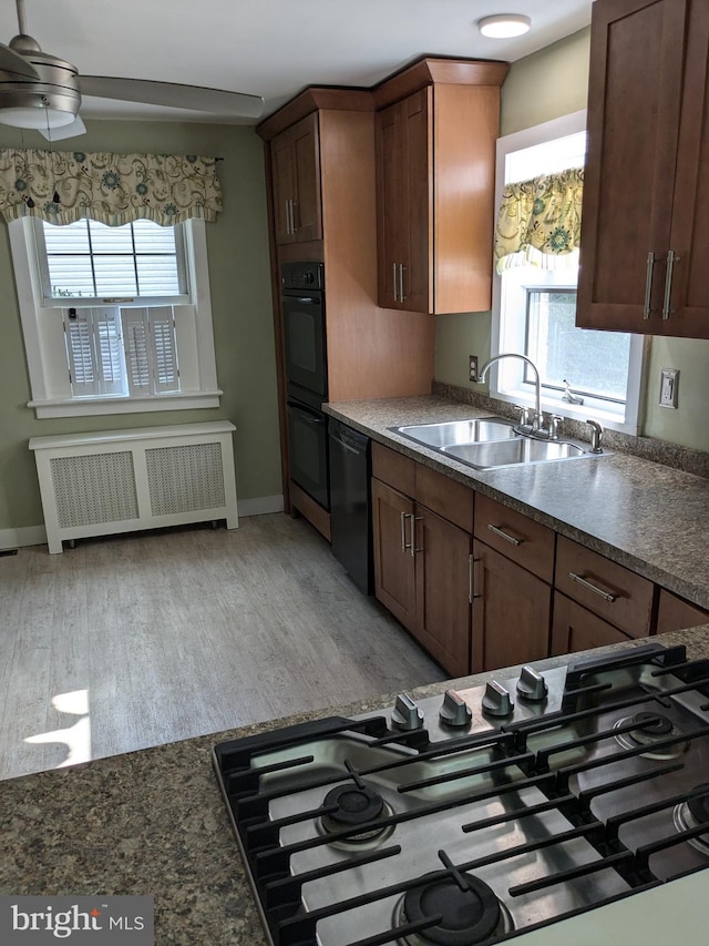 kitchen featuring light hardwood / wood-style floors, sink, black appliances, radiator heating unit, and ceiling fan