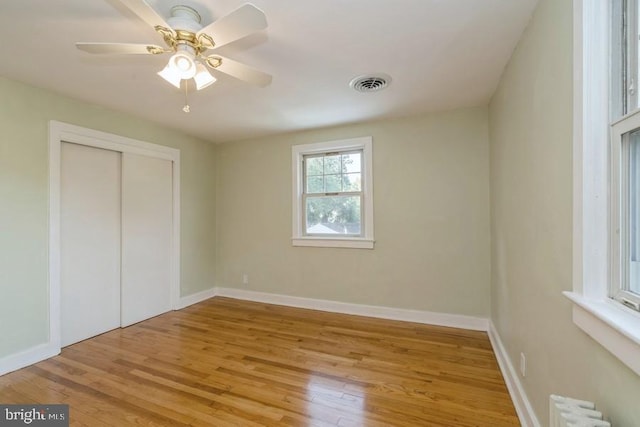 unfurnished bedroom featuring light hardwood / wood-style flooring, a closet, ceiling fan, and radiator