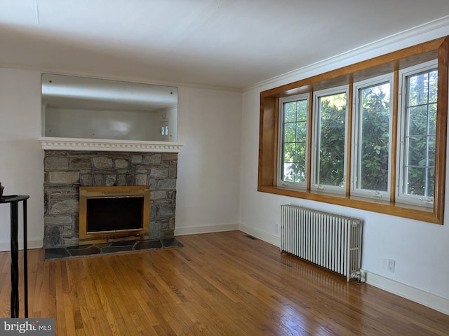 unfurnished living room featuring a stone fireplace, hardwood / wood-style flooring, crown molding, and radiator heating unit