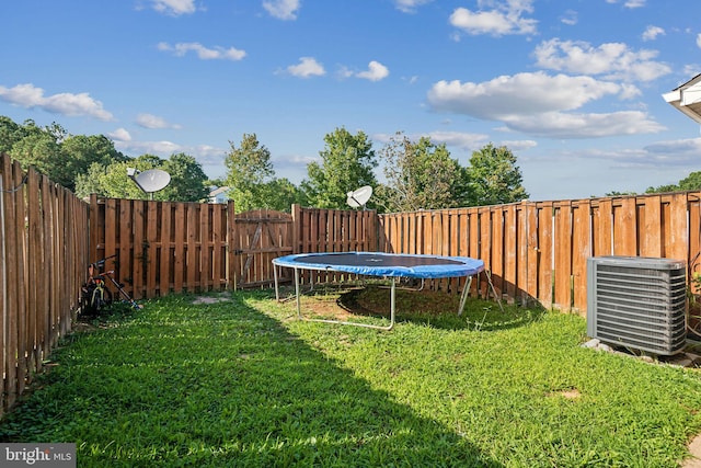 view of yard with a trampoline, central AC, and a fenced backyard