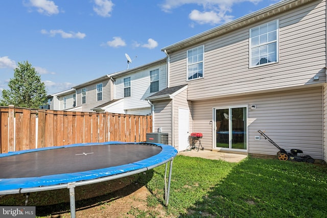 back of property featuring a trampoline, a yard, central air condition unit, a patio area, and fence