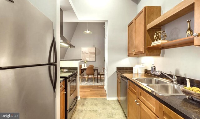 kitchen with hanging light fixtures, sink, wall chimney range hood, appliances with stainless steel finishes, and light wood-type flooring