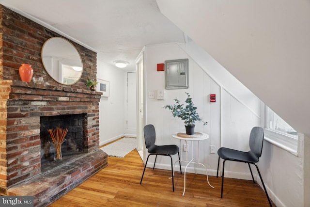 living area with electric panel, a brick fireplace, baseboards, and wood finished floors