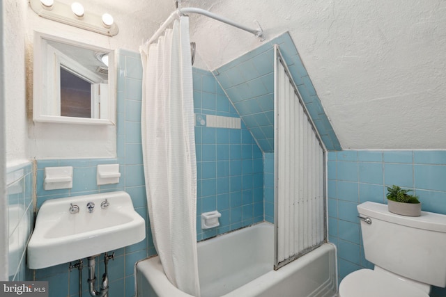 bathroom with tile walls, toilet, shower / tub combo with curtain, and a sink