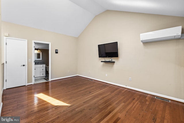 unfurnished bedroom with connected bathroom, hardwood / wood-style flooring, a wall unit AC, and lofted ceiling