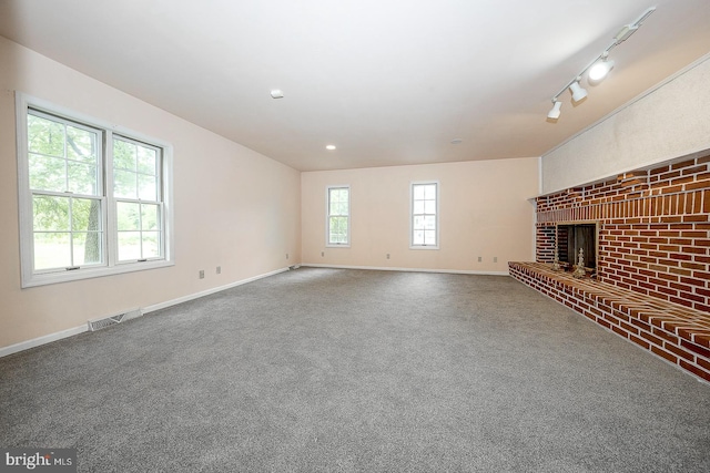 unfurnished living room featuring a brick fireplace, carpet floors, and rail lighting