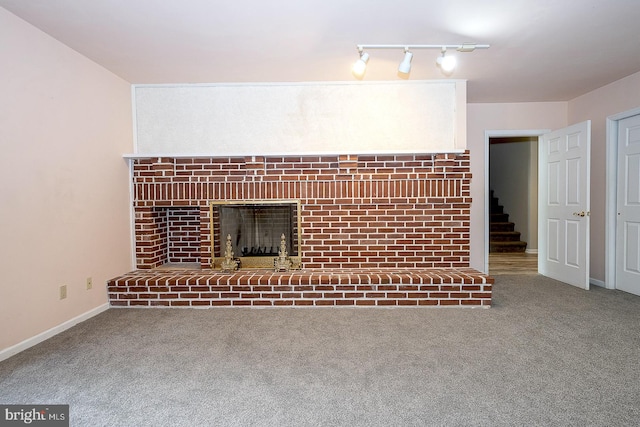 unfurnished living room featuring a fireplace, rail lighting, and carpet flooring