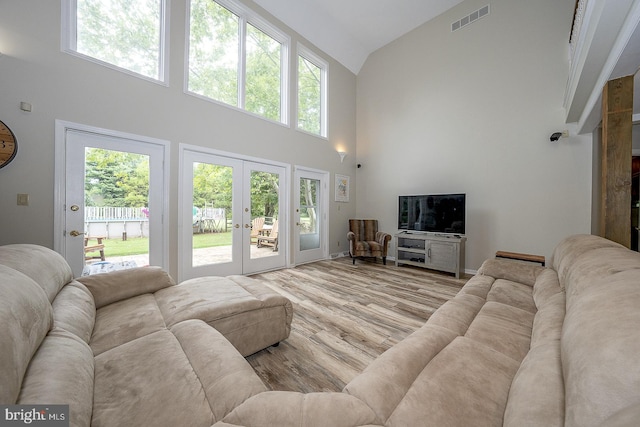 living room featuring french doors, light hardwood / wood-style floors, and high vaulted ceiling