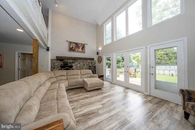 living room with french doors, a stone fireplace, a high ceiling, and light wood-type flooring