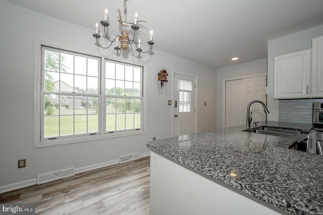 kitchen with backsplash, dark stone countertops, light wood-type flooring, a chandelier, and white cabinets