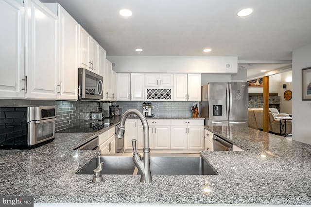 kitchen featuring decorative backsplash, appliances with stainless steel finishes, white cabinetry, dark stone counters, and sink