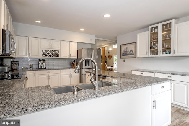 kitchen with black stovetop, backsplash, dark stone countertops, light wood-type flooring, and white cabinetry