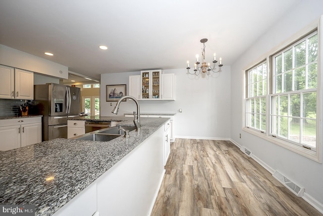 kitchen with appliances with stainless steel finishes, white cabinets, dark stone countertops, and decorative light fixtures