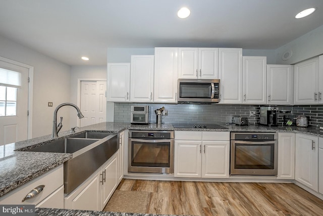 kitchen featuring white cabinets, stainless steel appliances, light wood-type flooring, and dark stone counters