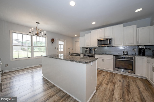 kitchen featuring appliances with stainless steel finishes, white cabinetry, a kitchen island with sink, a chandelier, and light hardwood / wood-style floors