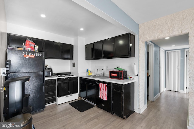 kitchen with light wood-style flooring, light countertops, dark cabinetry, black appliances, and a sink