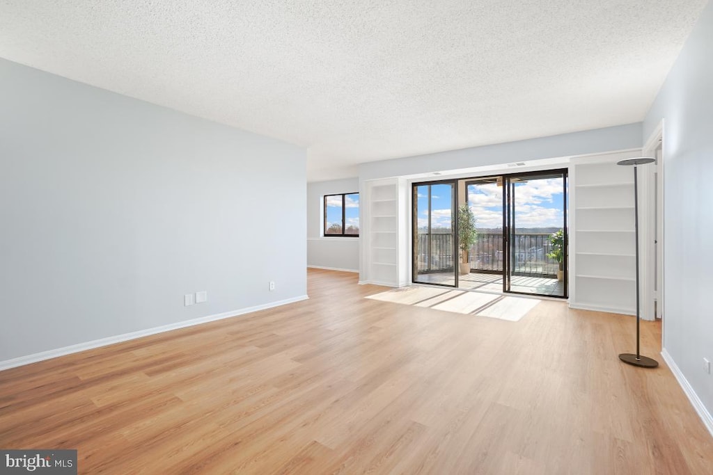 unfurnished living room featuring a textured ceiling, wood finished floors, and baseboards