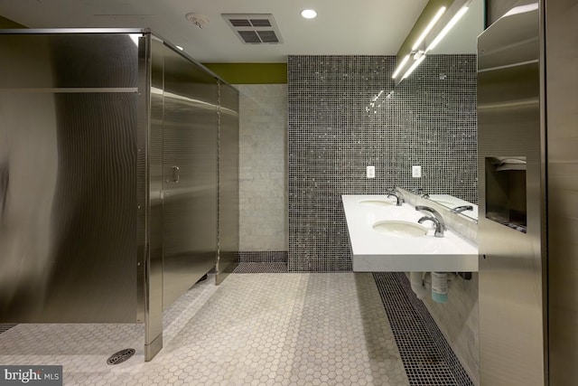 bathroom with tiled shower, double sink, and tile walls