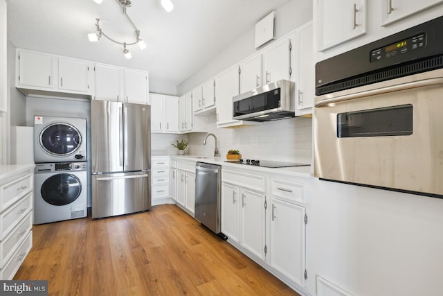 kitchen featuring white cabinets, light hardwood / wood-style floors, stacked washer / dryer, and appliances with stainless steel finishes